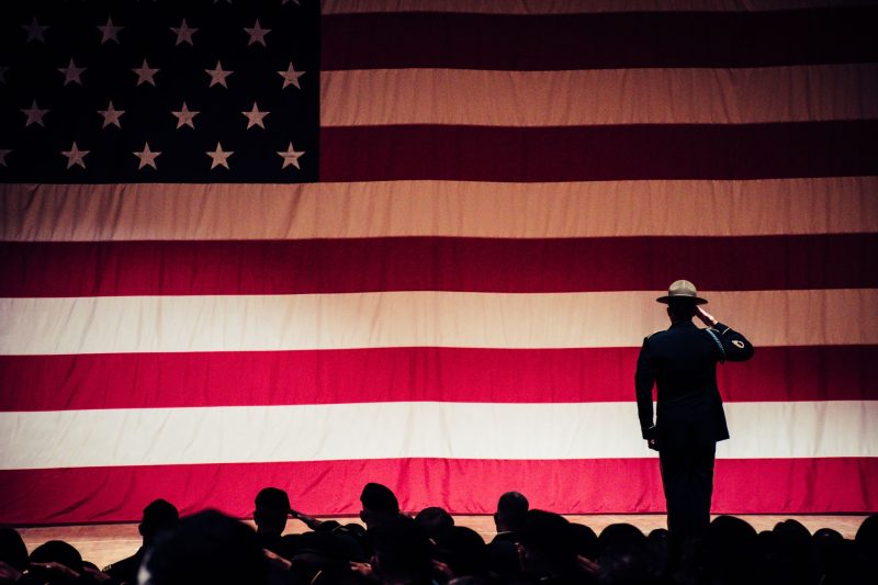 Soldier saluting the American flag during a formal ceremony in an auditorium.