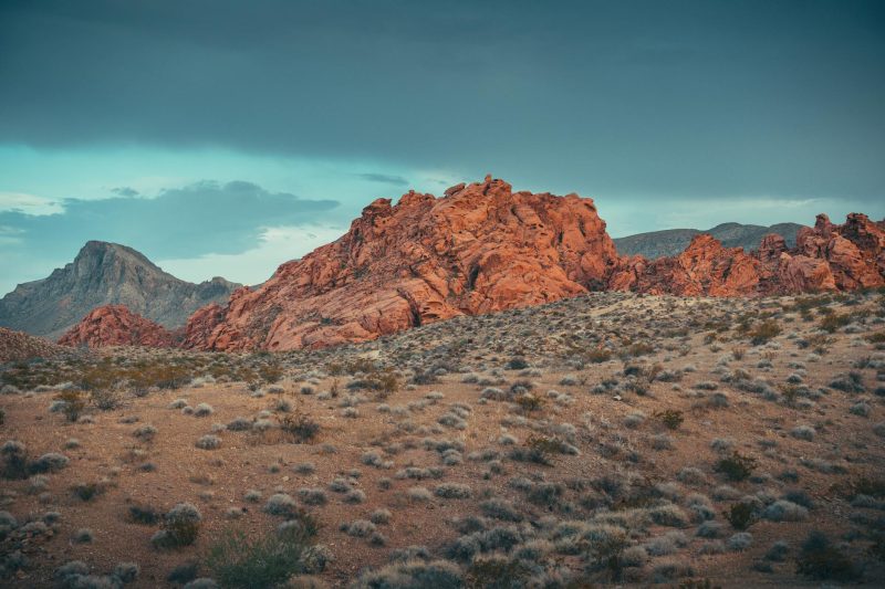 Red rock formations silhouetted against a moody twilight sky in a tranquil desert landscape.