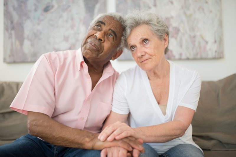 Elderly couple sitting closely together, sharing a loving embrace in a cozy indoor setting.